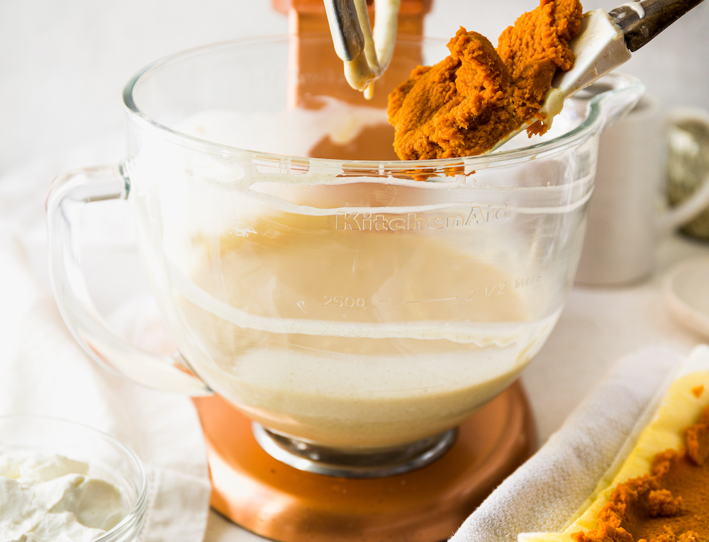 Adding pumpkin puree to the bowl of a stand mixer.