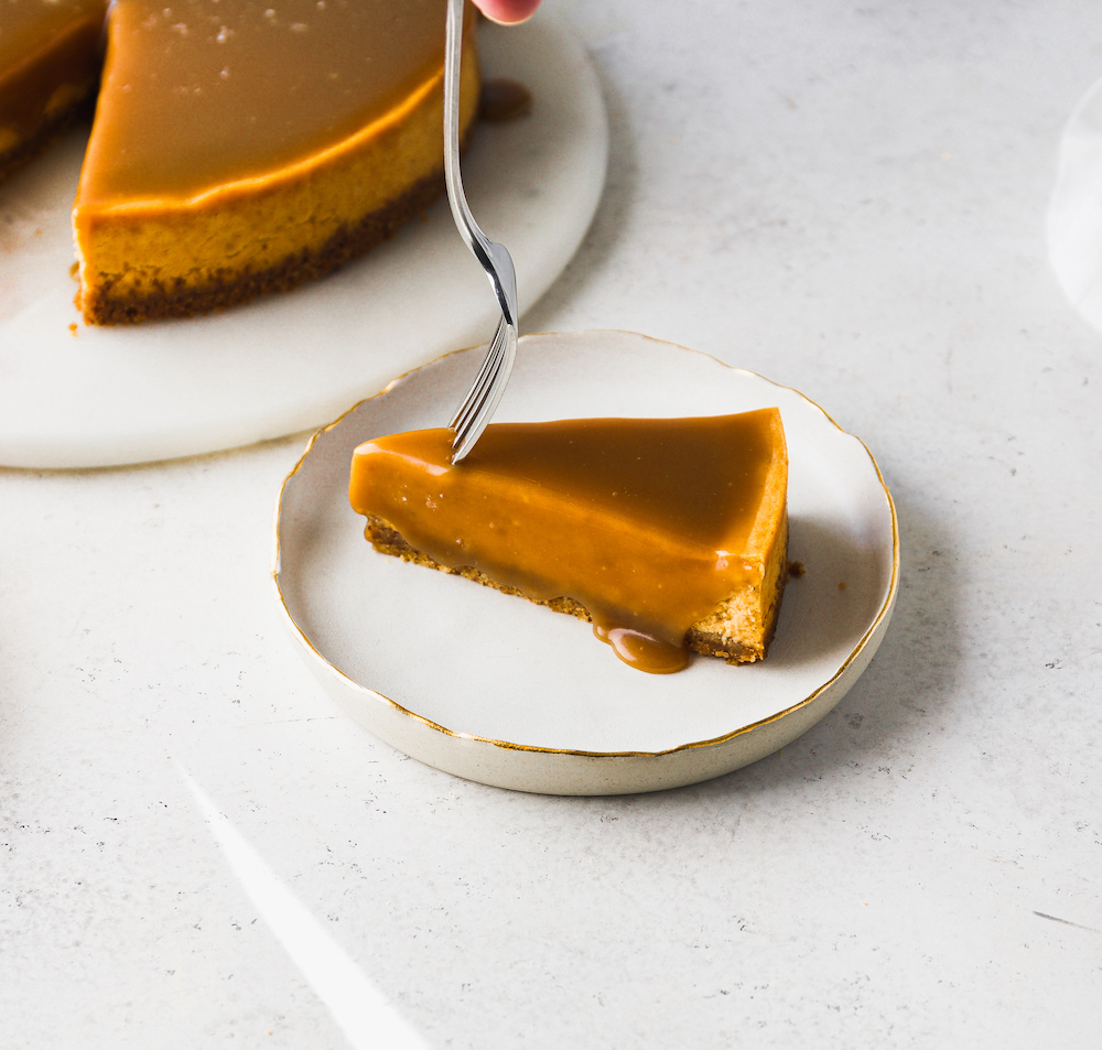 A fork getting a bite out of a slice of pumpkin cheesecake.