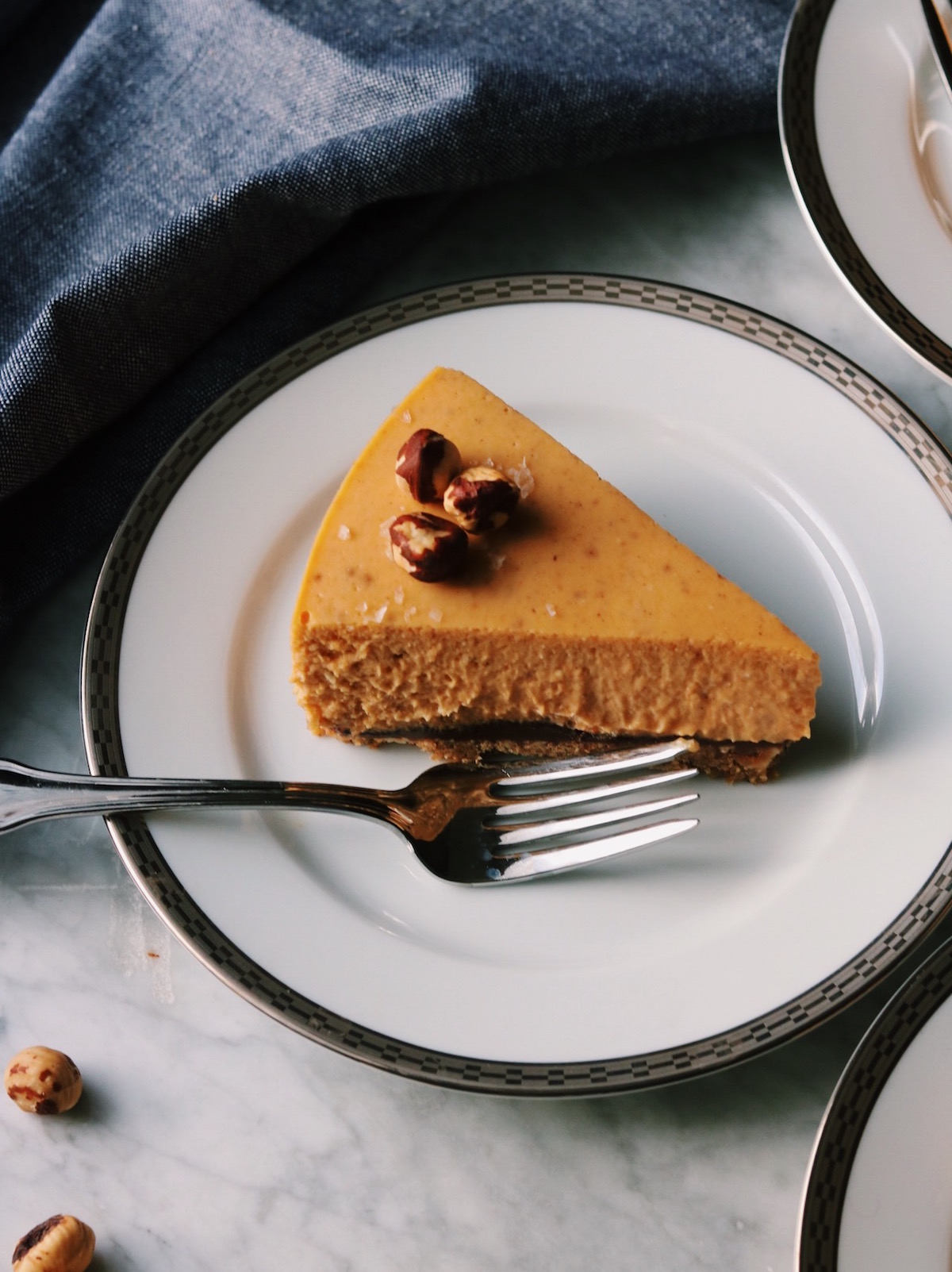 Close up of a slice of pumpkin cheesecake with hazelnuts on top.