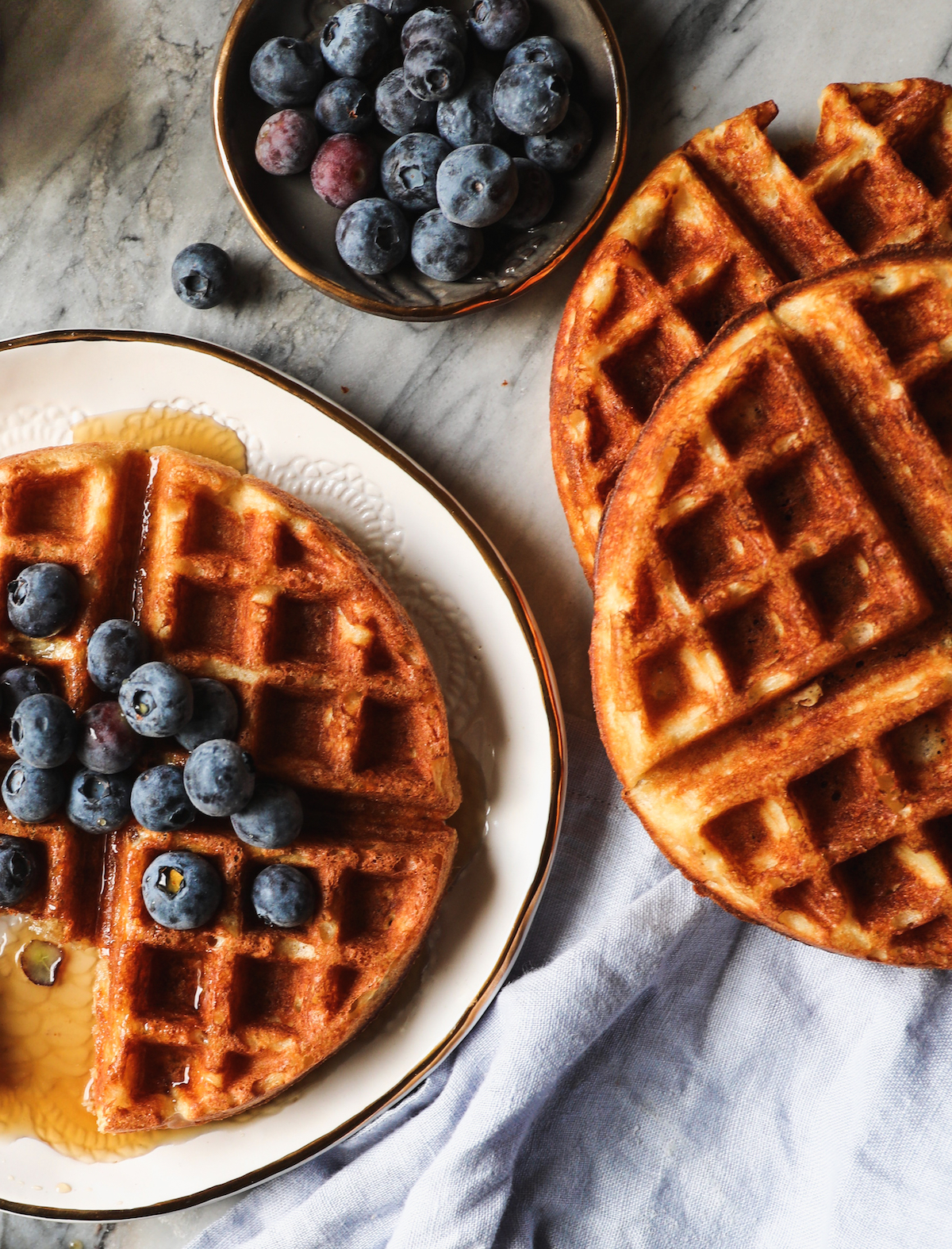 An overhead shot of crispy buttermilk waffles with blueberries and syrup.