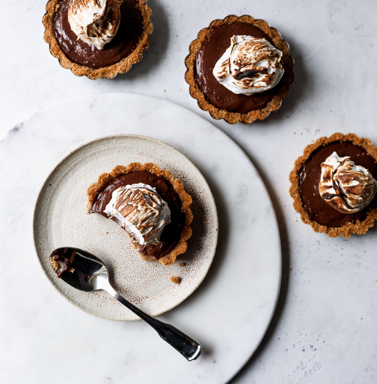 Four finished s'mores tarts with one on a plate.