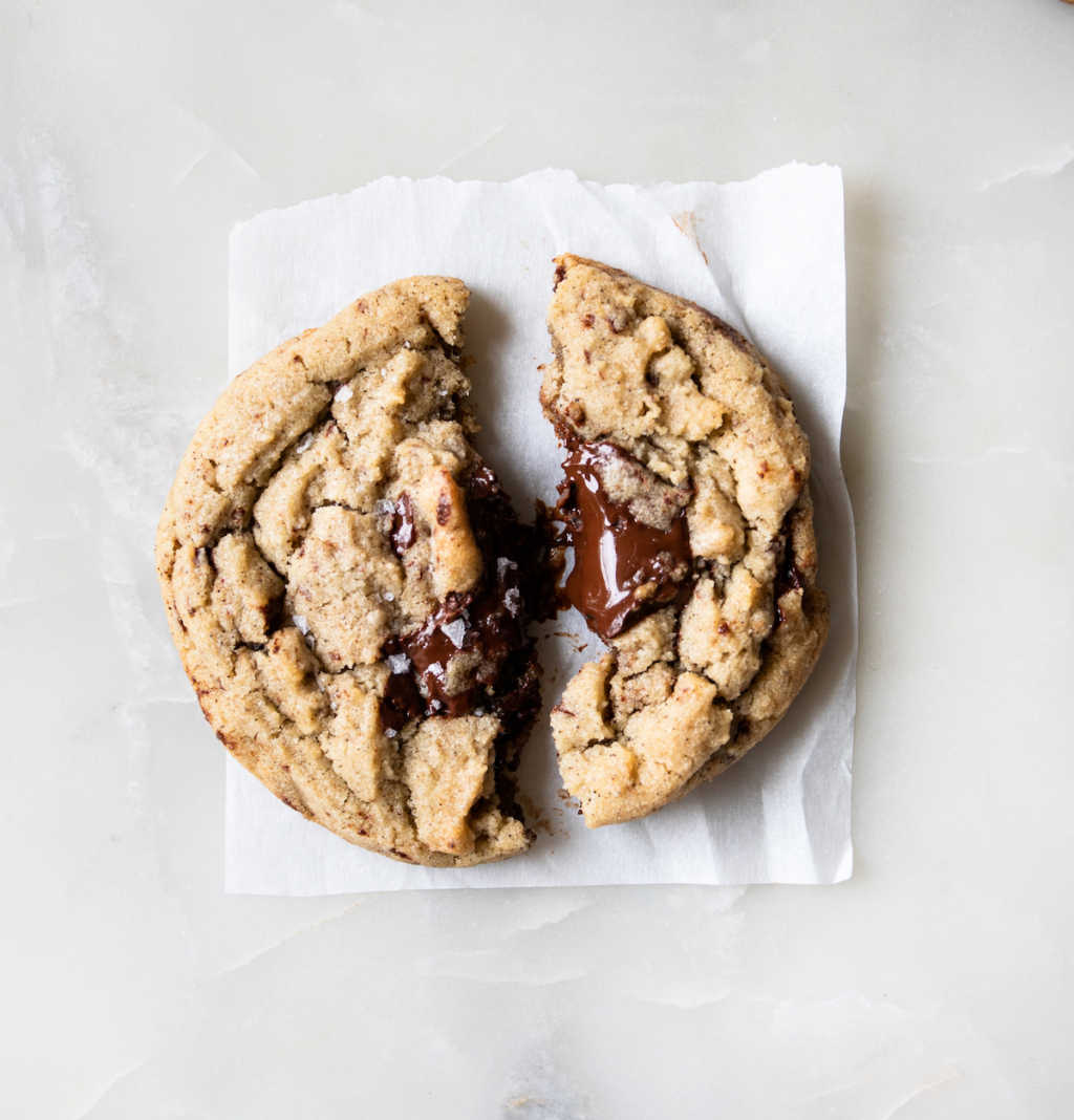 A cookie broken in half with warm glossy chocolate.