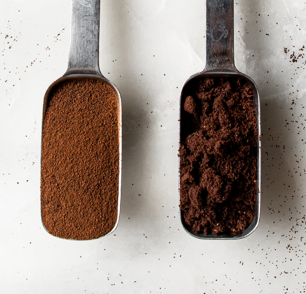 Two measuring spoons, one holding espresso powder and the other holding finely-ground espresso.