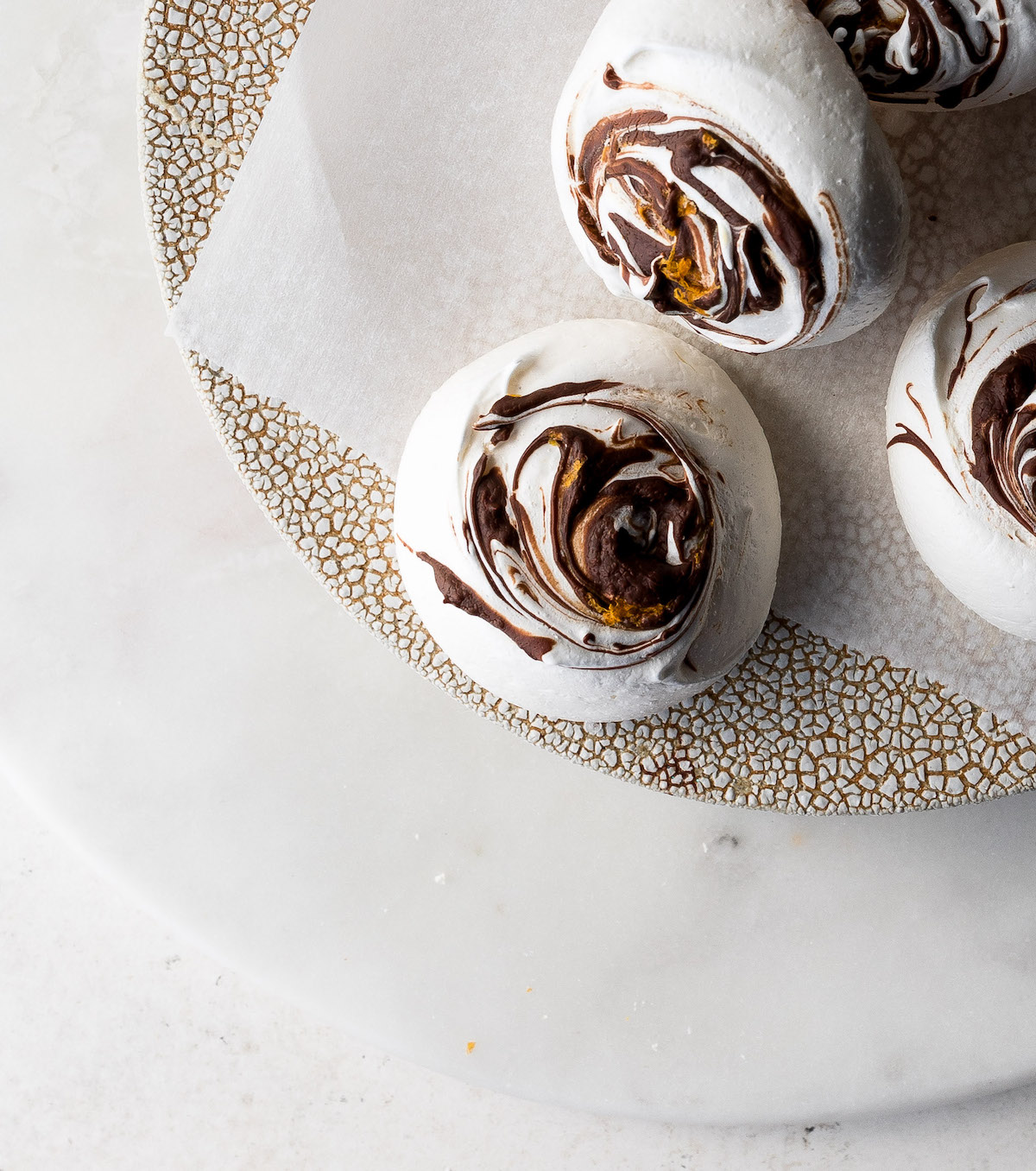 Meringue cookies with chocolate and orange zest swirls over the tops on a platter.