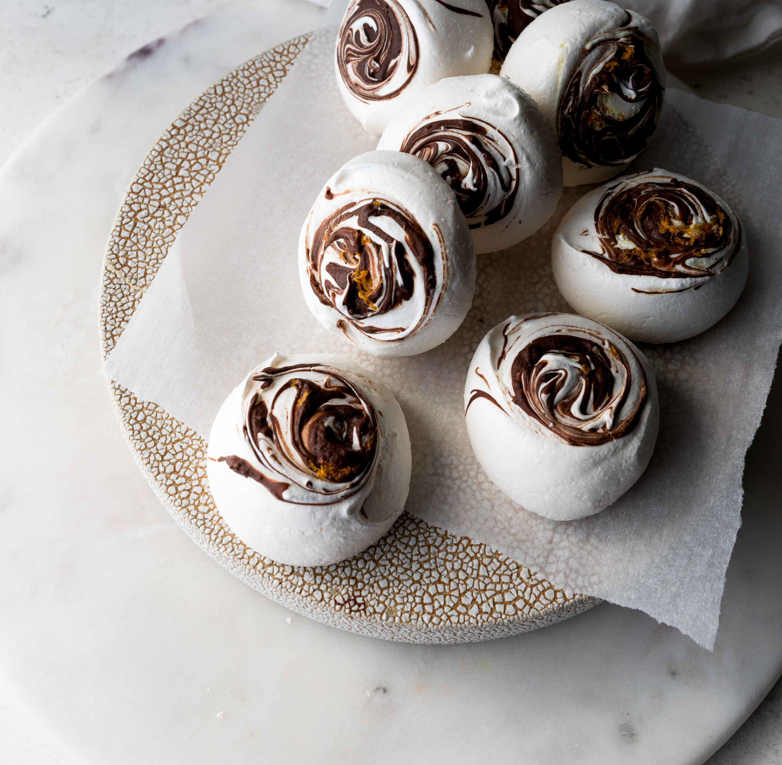 Chocolate Orange Meringues on a parchment lined platter on top of a marble surface.