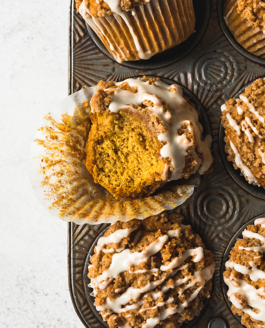 A close up of a pumpkin muffin with a  bite out of it in a muffin tin.