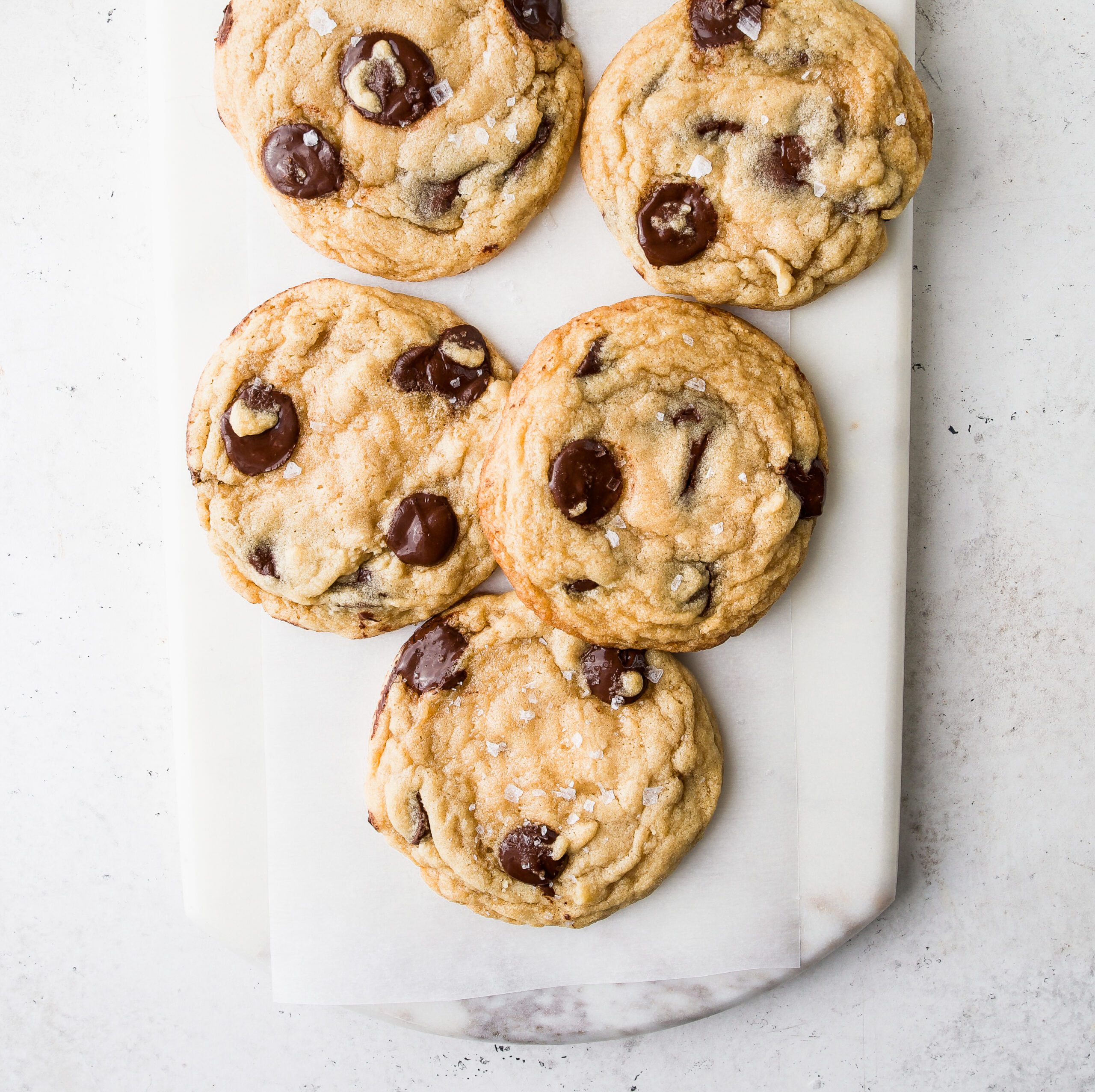 Five chocolate chip cookies on a white marble surface.