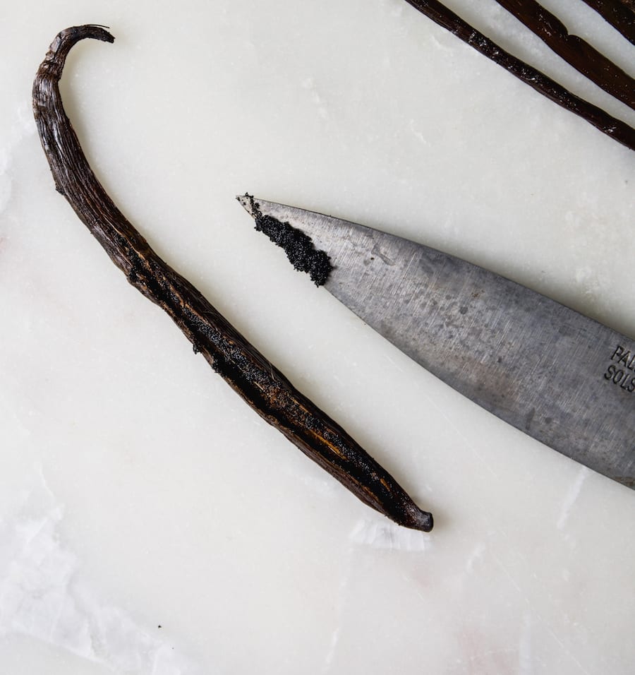 One scraped vanilla bean pod and the tip of a knife with vanilla bean seeds on it.
