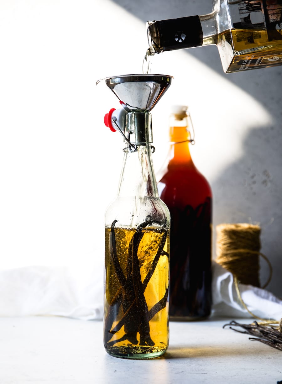 Pouring alcohol into a glass bottle that is filled with  vanilla bean pods. 