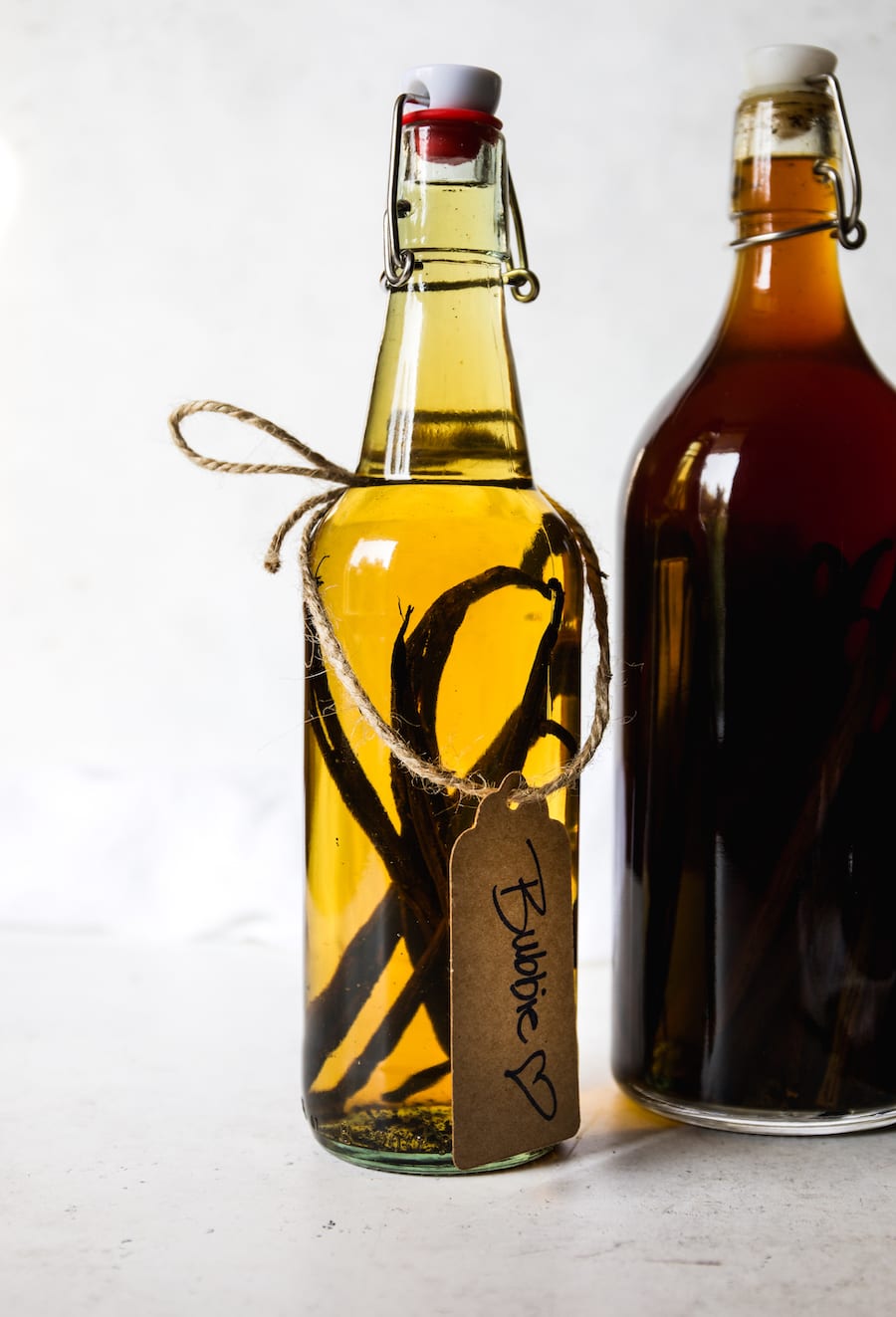 Two glass bottles of vanilla bean extract and one with a gift tag hanging down the side.