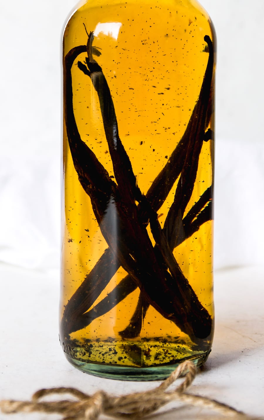 A close up of a glass bottle that is filled with bourbon and vanilla bean pods. You  can see vanilla bean flecks.