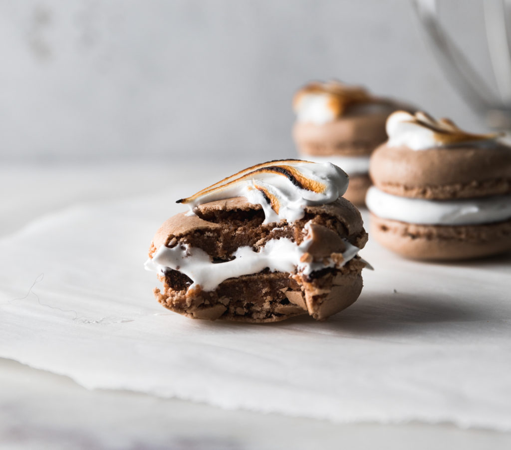 A chocolate French macaron with marshmallow filling with a big bite out of it