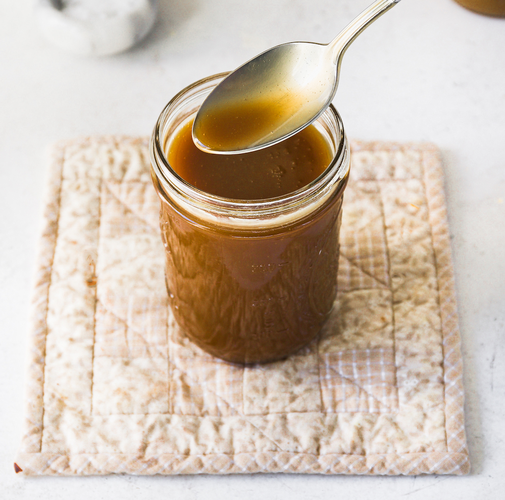 A jar with caramel  sauce and a  spoon over it.