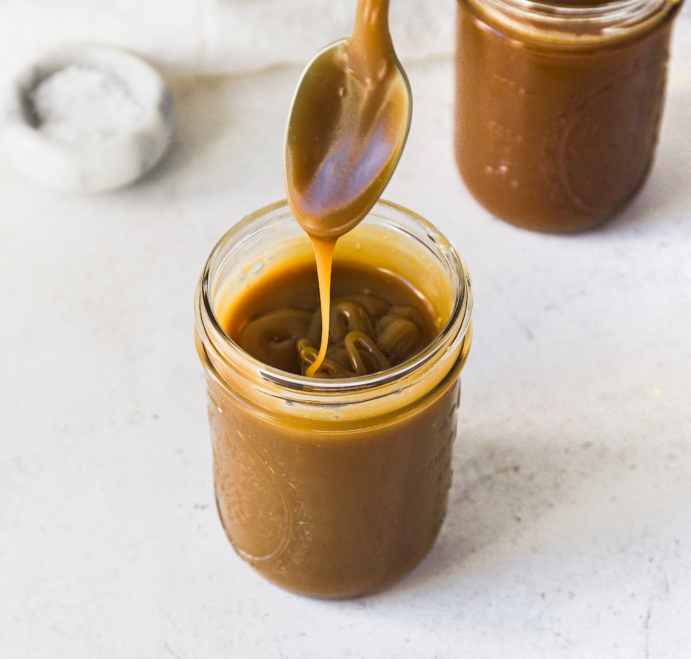 A jar of caramel sauce with a spoon drizzling it into the jar.