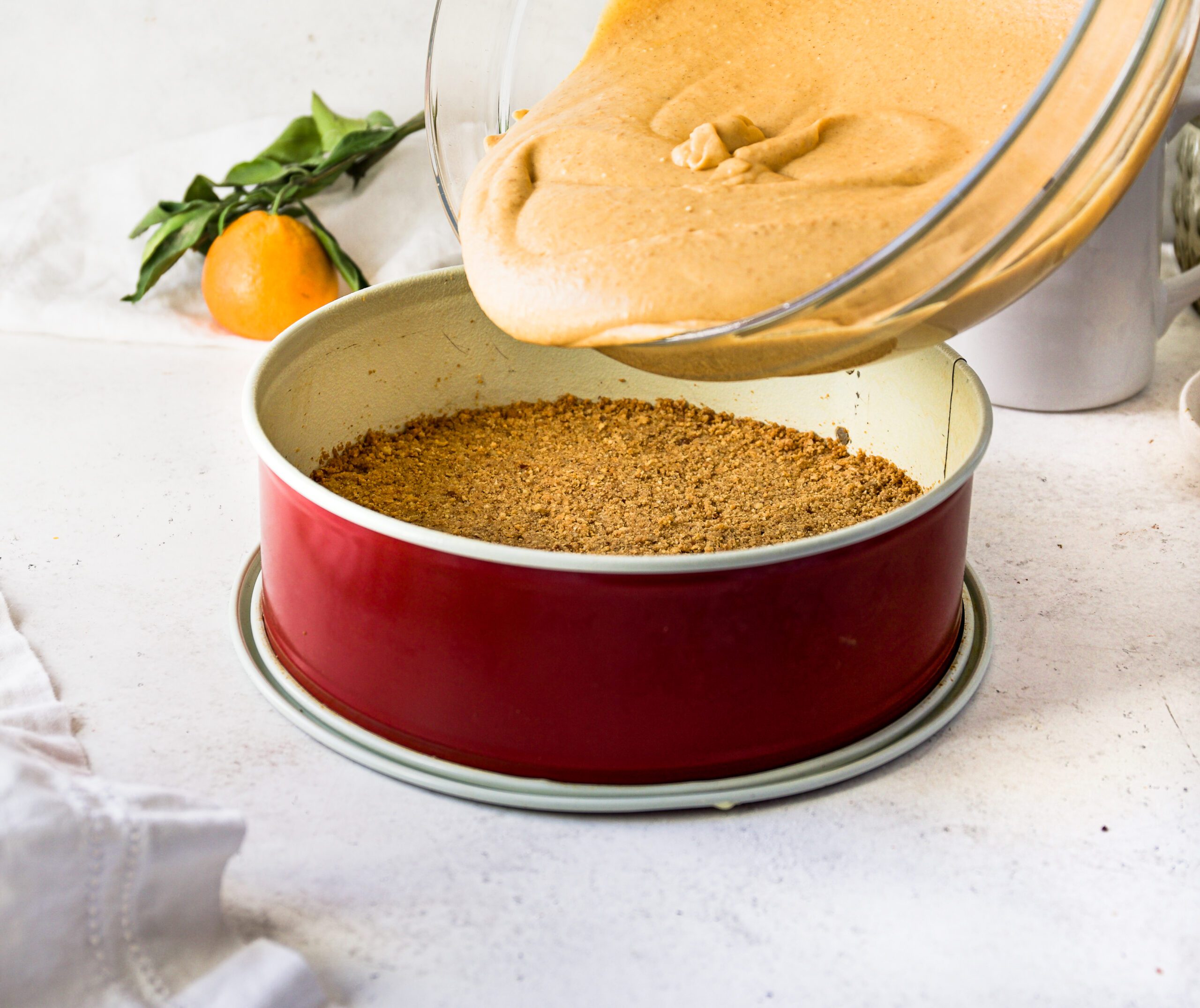 Pouring pumpkin cheesecake filling into a cooked graham cracker crust.