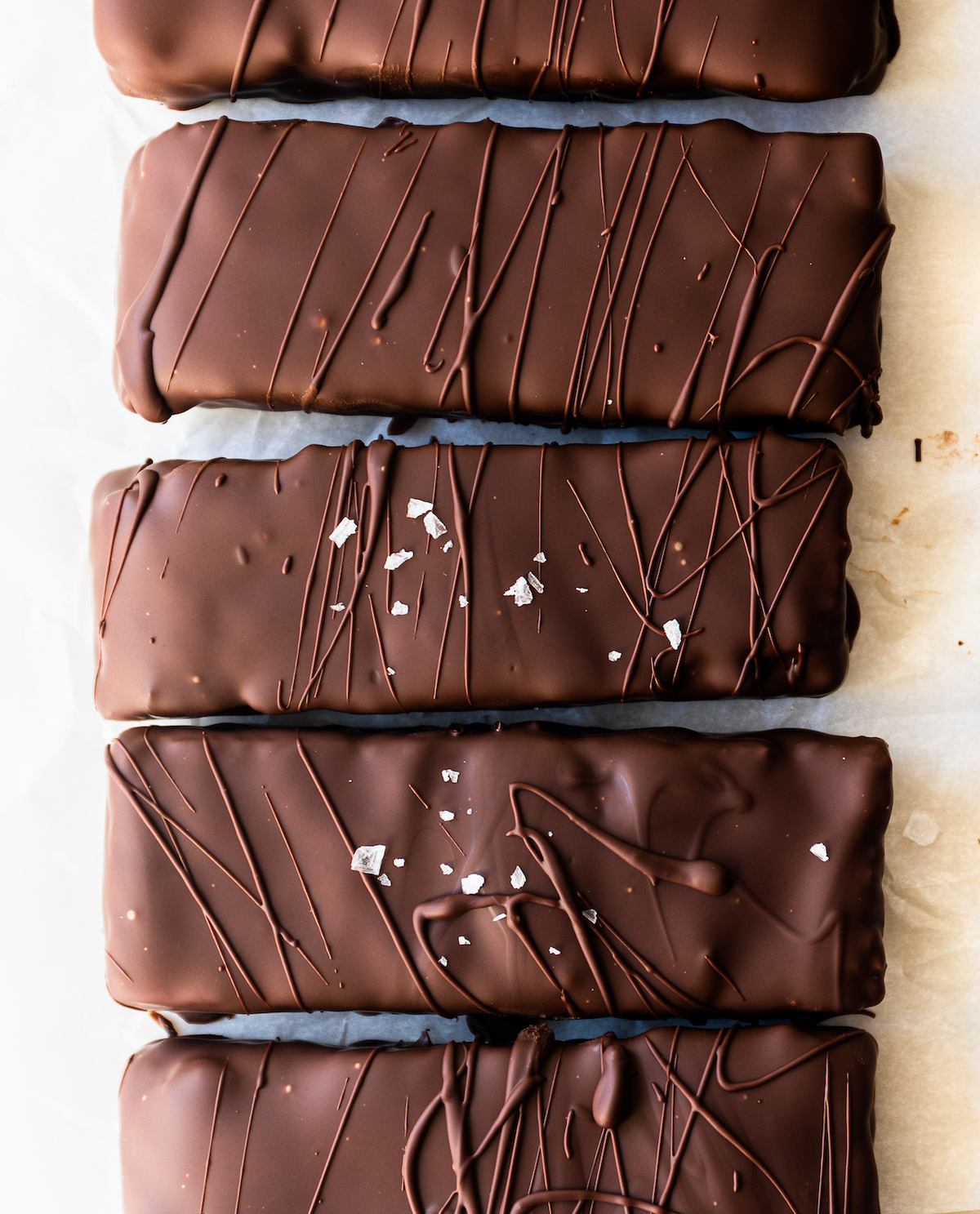 A close up of five bars covered in chocolate with sea salt sprinkled over the top.