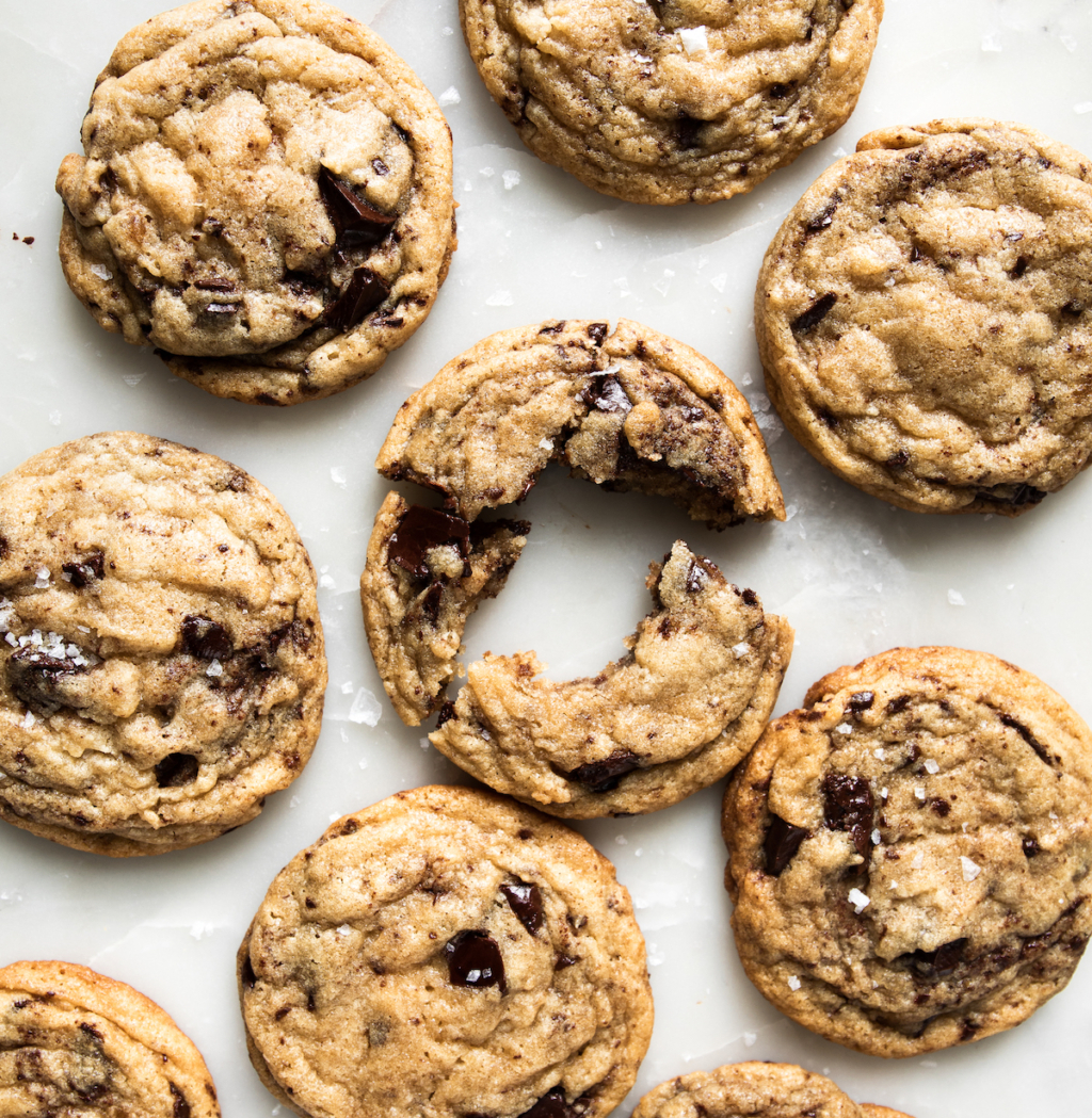 A bunch of chocolate cookies on a white background with one with a bite out of it.