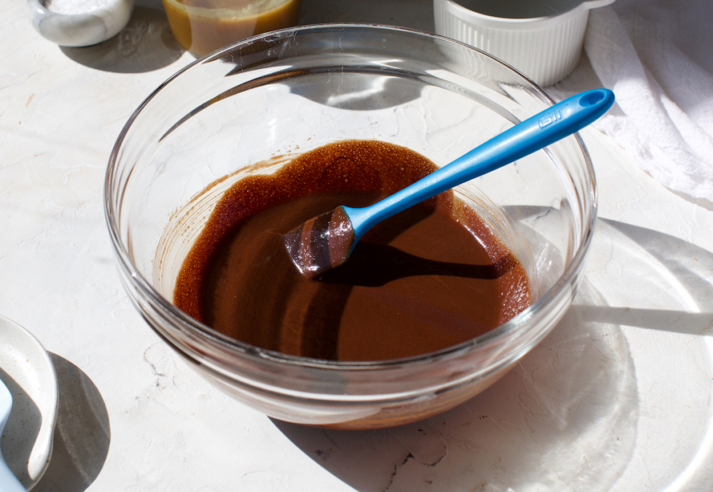 Melted chocolate in  glass bowl with a blue spatula. 
