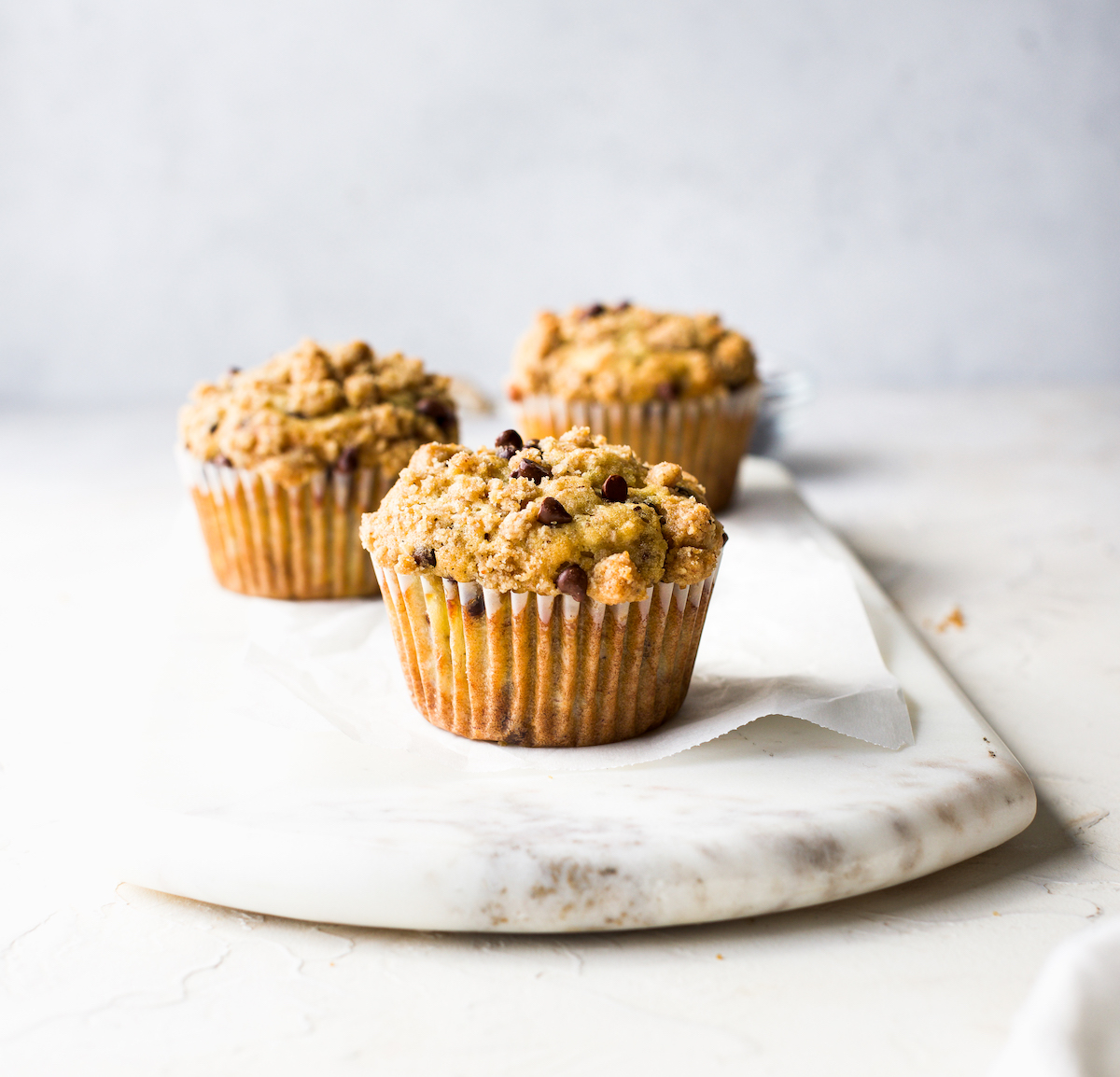 Three banana streusel muffins on a marble serving board.