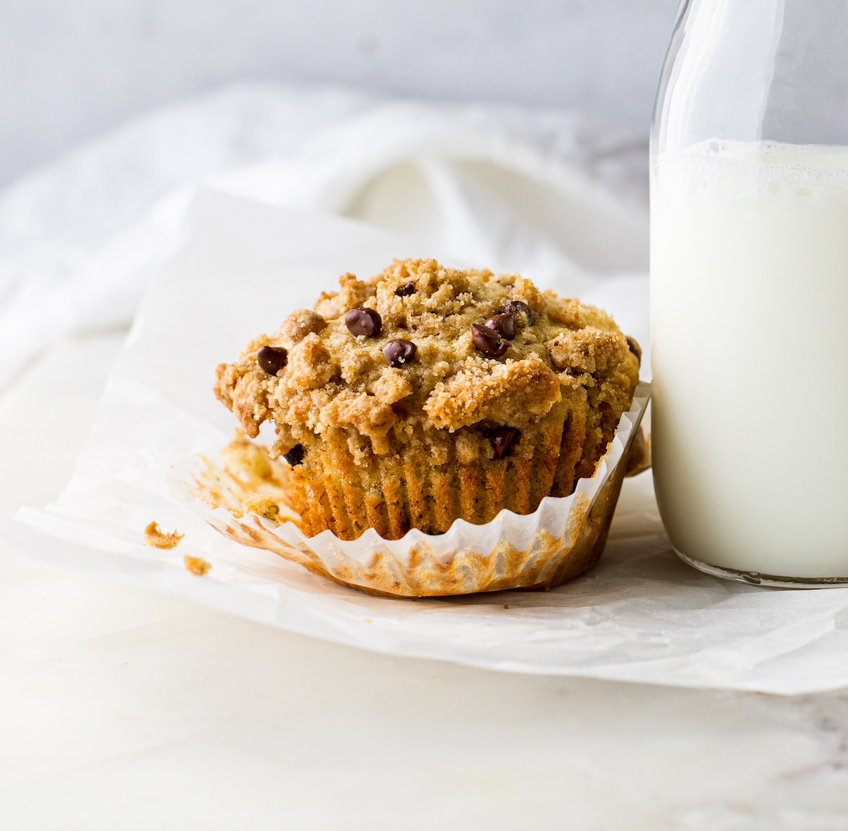 A close up of a muffin with the wrapper pulled down with a white background.