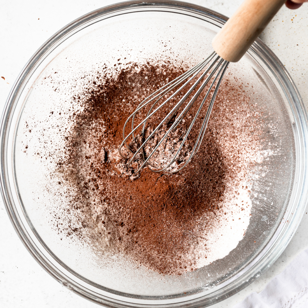 A glass bowl with flour, cocoa powder, baking powder and salt.