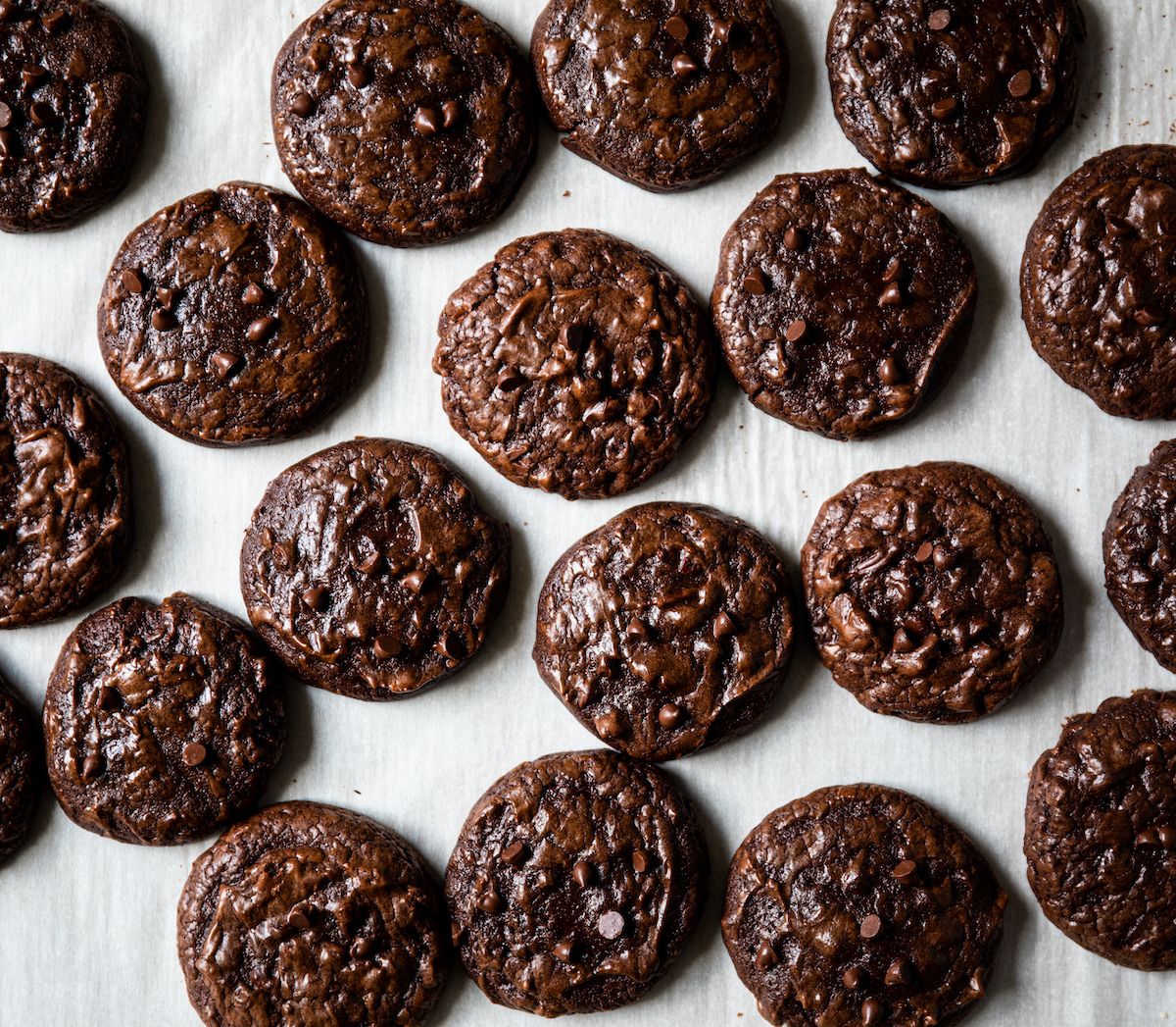 Lots of dark chocolate cookies on a white surface.