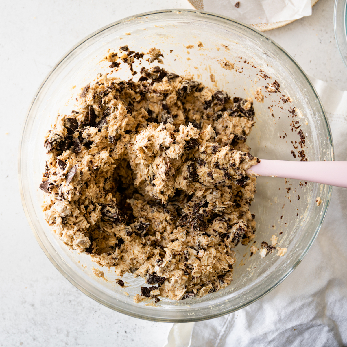A glass bowl on a white surface with the best oatmeal chocolate chip cookie dough!