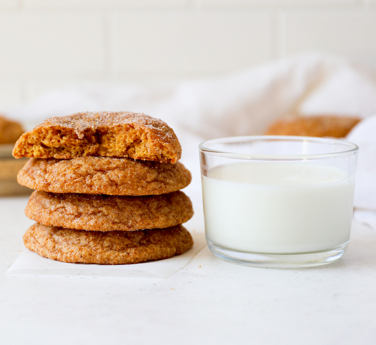 Four brown butter pumpkin snickerdoodles cookies, one with a bite out of it next to a glass of milk.
