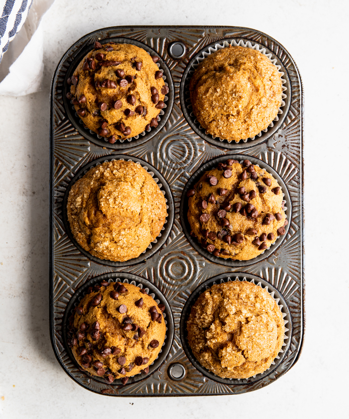 Pumpkin muffins in a tin on a white surface.