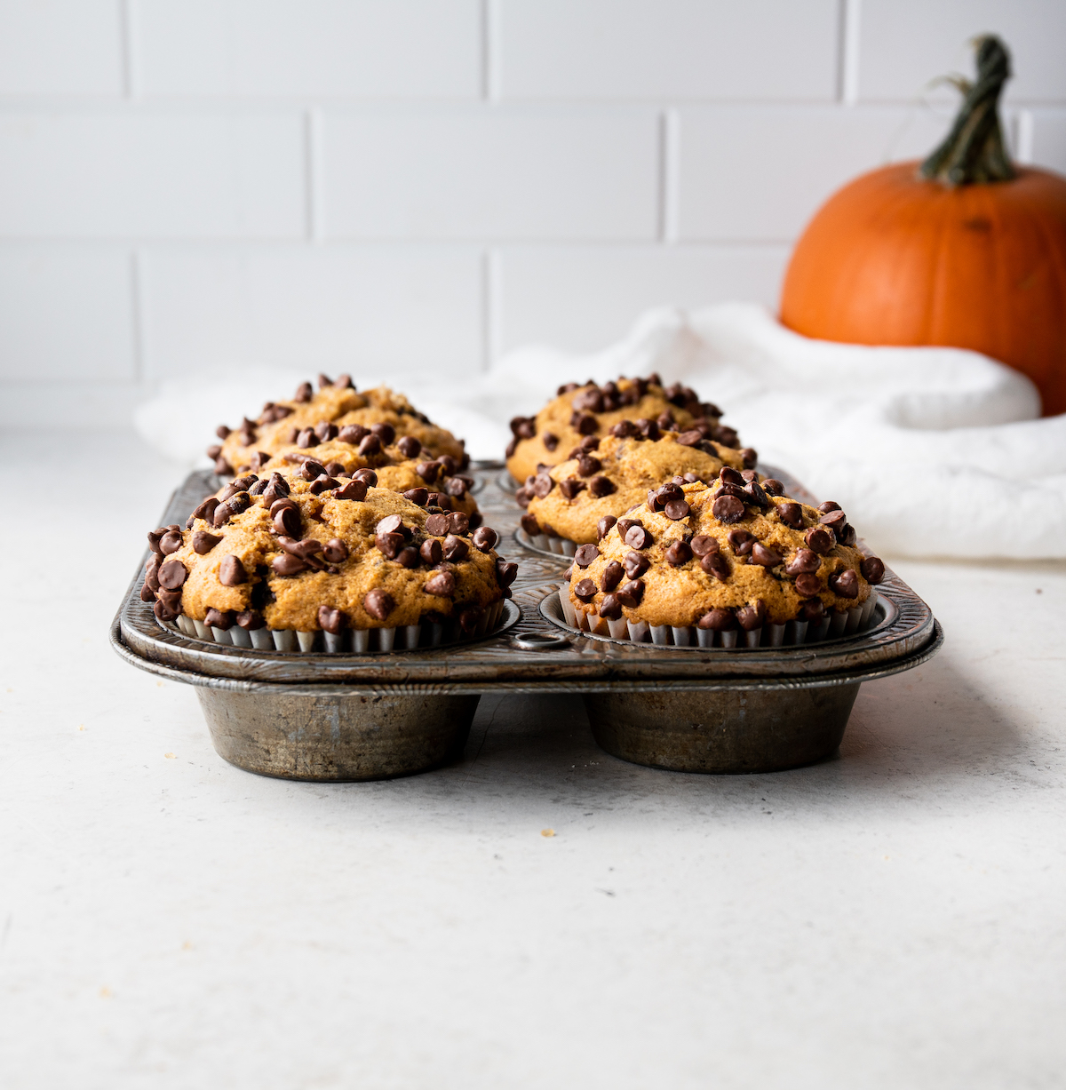 Pumpkin muffins with chocolate chips over the tops in a muffin pan.