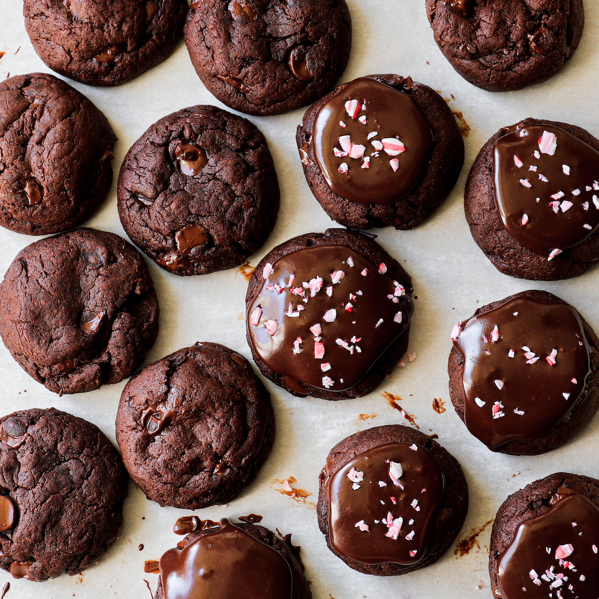 A bunch of chocolate cookies, some with frosting and some with crushed peppermint candies.