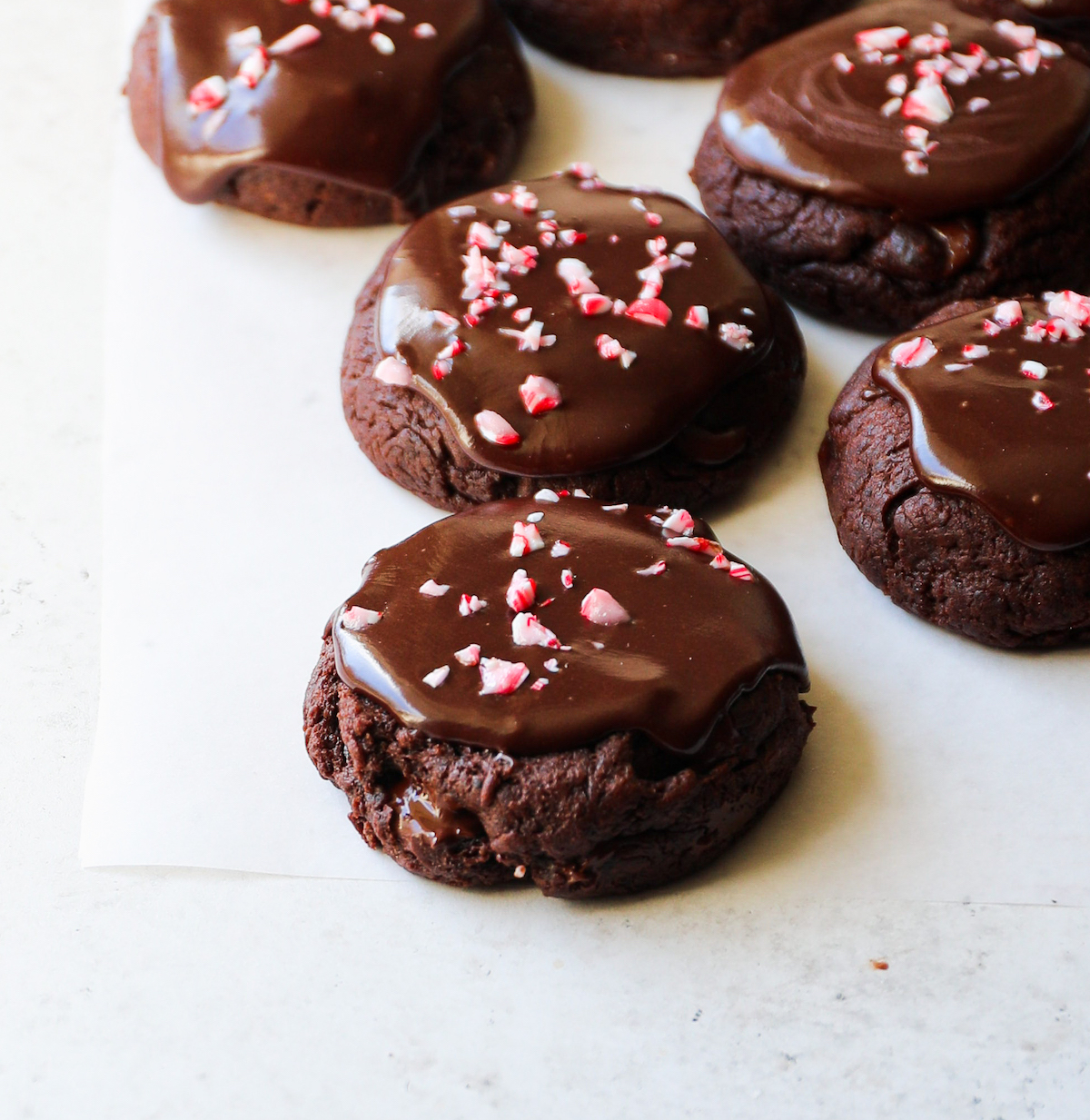 A close up side angle of chocolate cookies with frosting and candy canes.