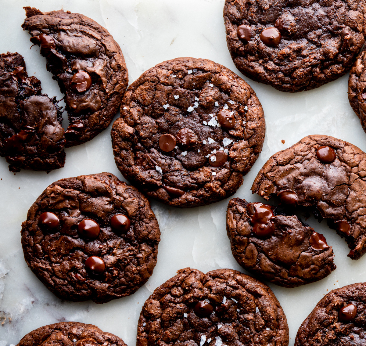 A bunch of chocolate cookies on a white surface with sea salt flakes.