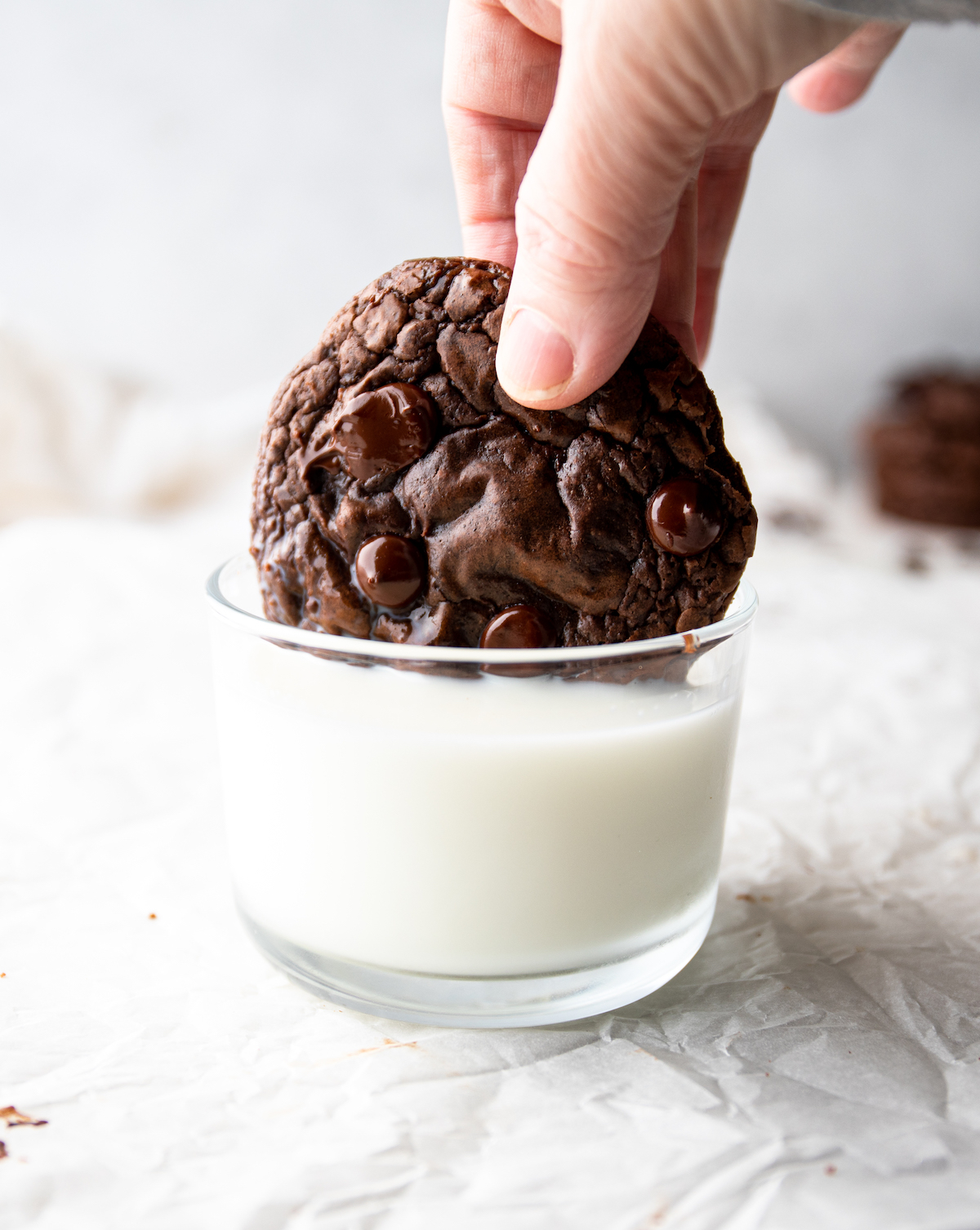 A hand dipping a chocolate cookie in a glass of milk.