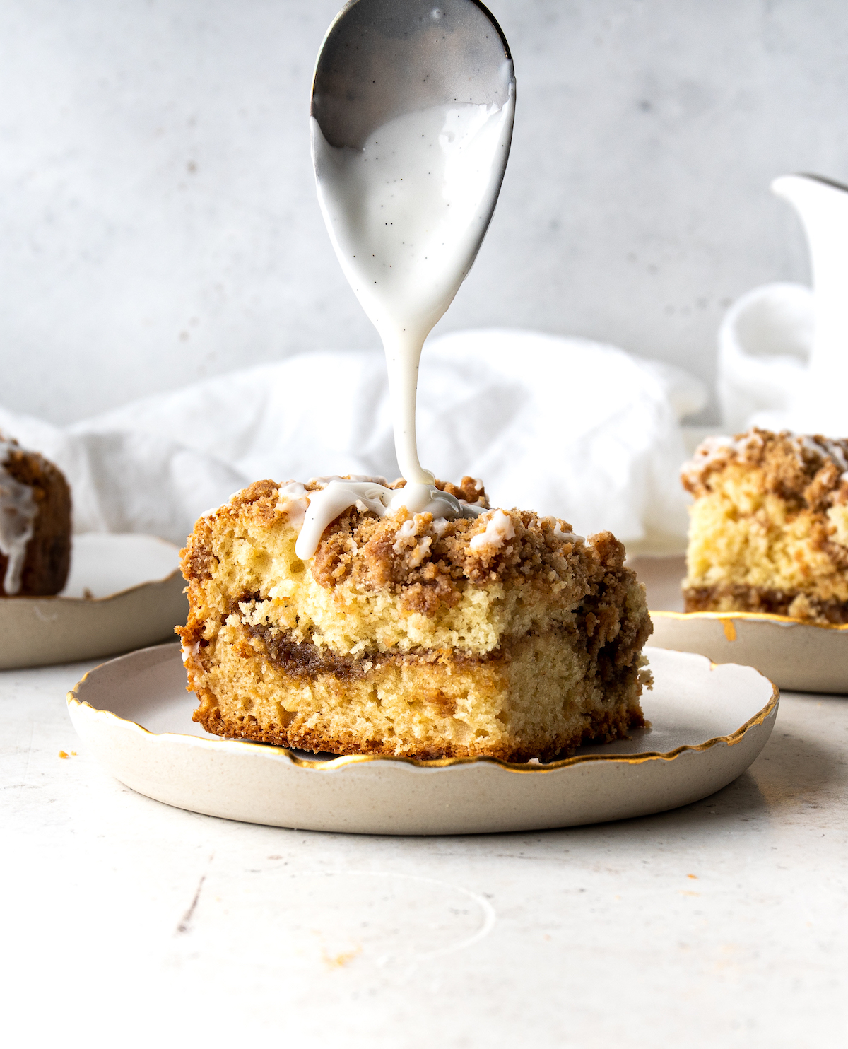 A coffee cake getting vanilla bean drizzle over the streusel top.