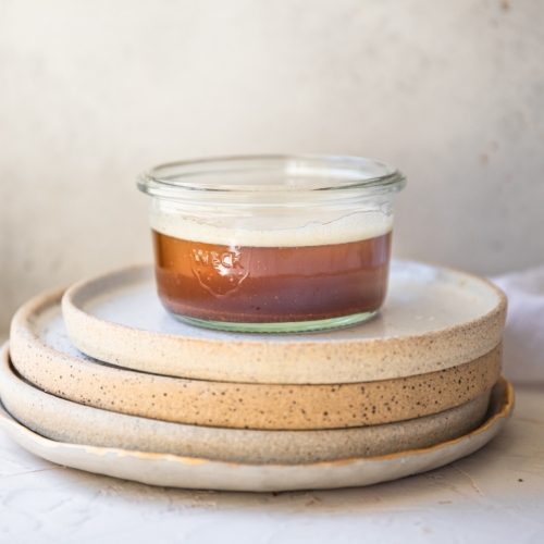 A glass ramekin of brown butter on top of some plates.