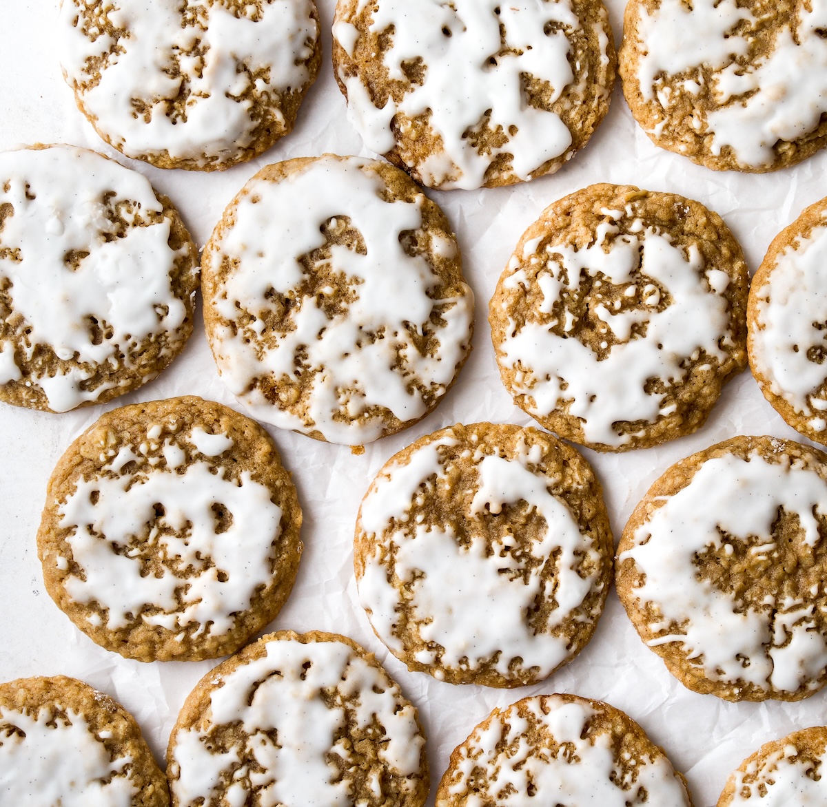An overhead shot of a bunch of iced oatmeal cookies on a white surface.
