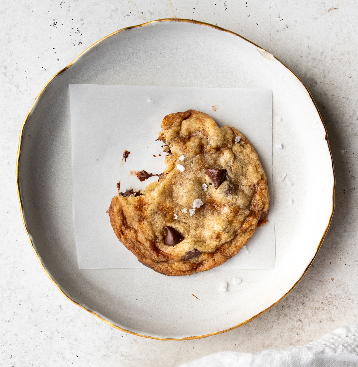 A bite out of a cookie on a piece of parchment paper on a plate.