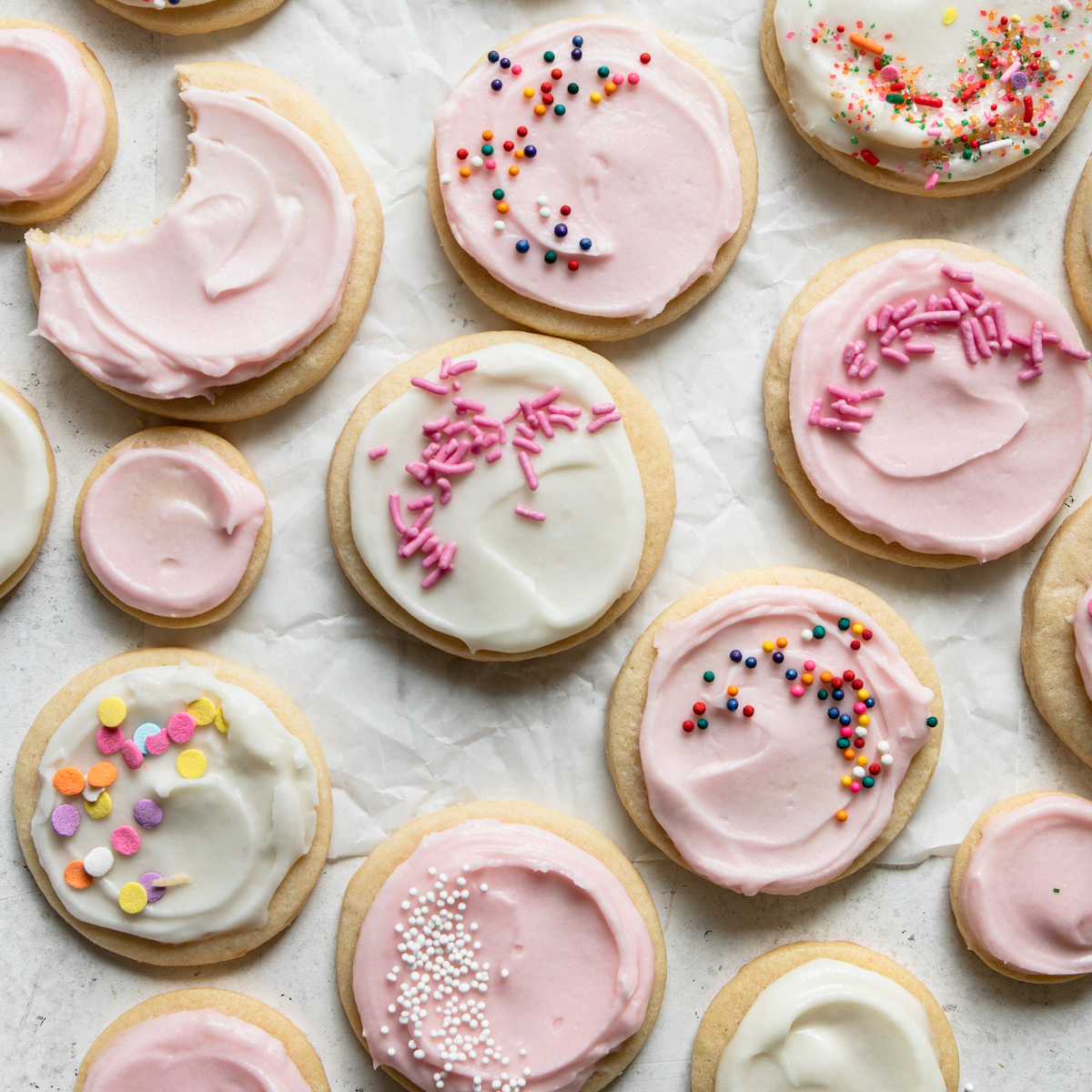 White crinkled parchment paper with a bunch of sugar cookies with sprinkles on top.I 