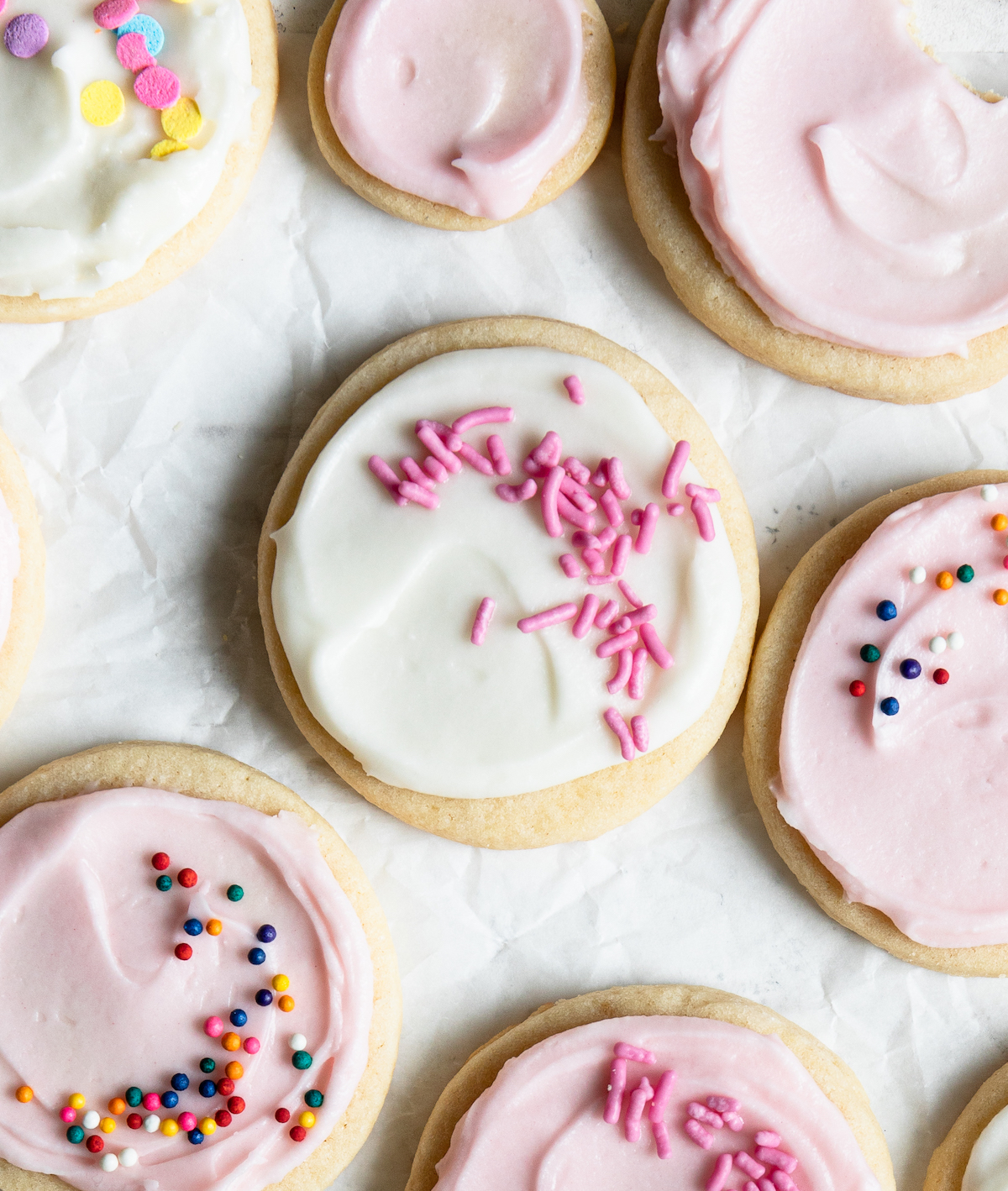 On a white surface, a bunch of sugar cookies with sprinkles.