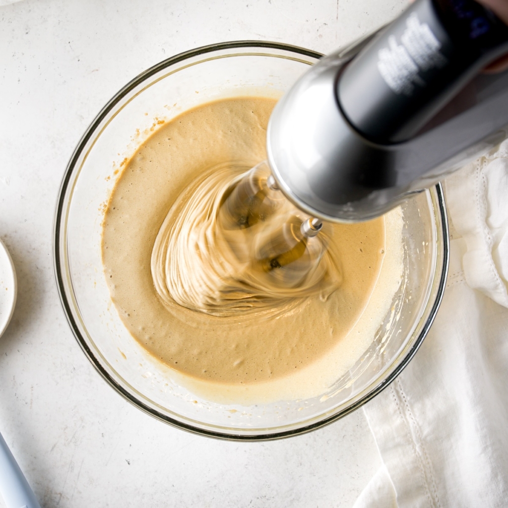 A handmixer mixing blondie dough in a glass bowl.