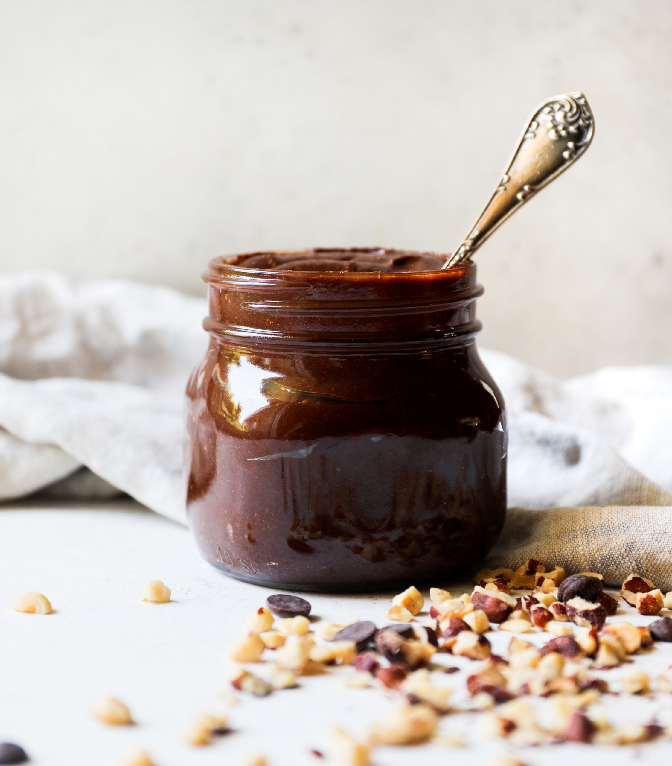 Nutella in a jar with hazelnuts on the white table.
