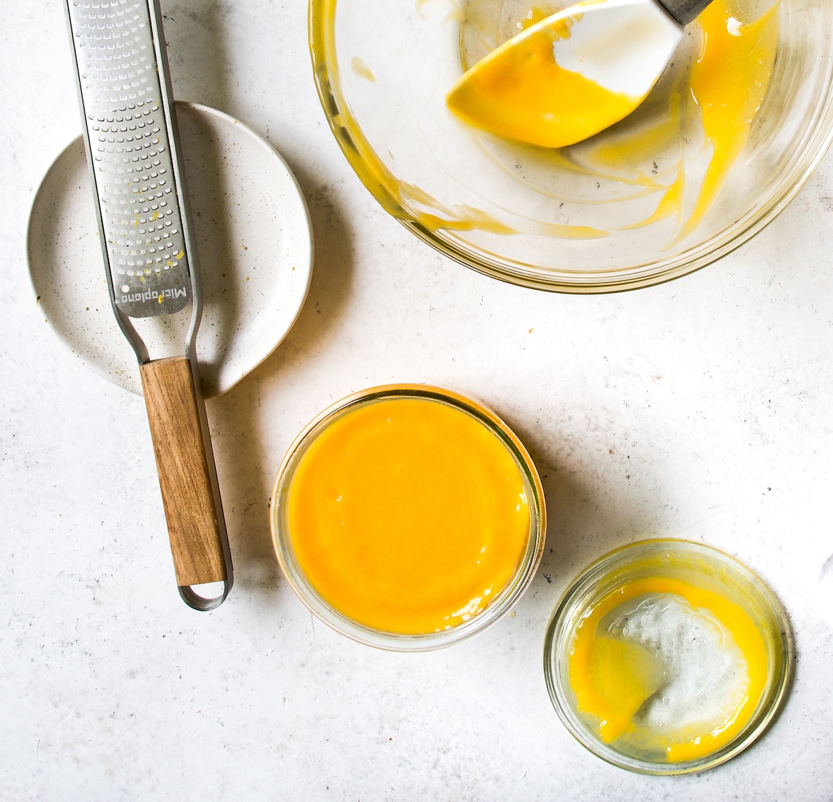 A glass bowl with lemon curd, a jar with curd on a white surface.