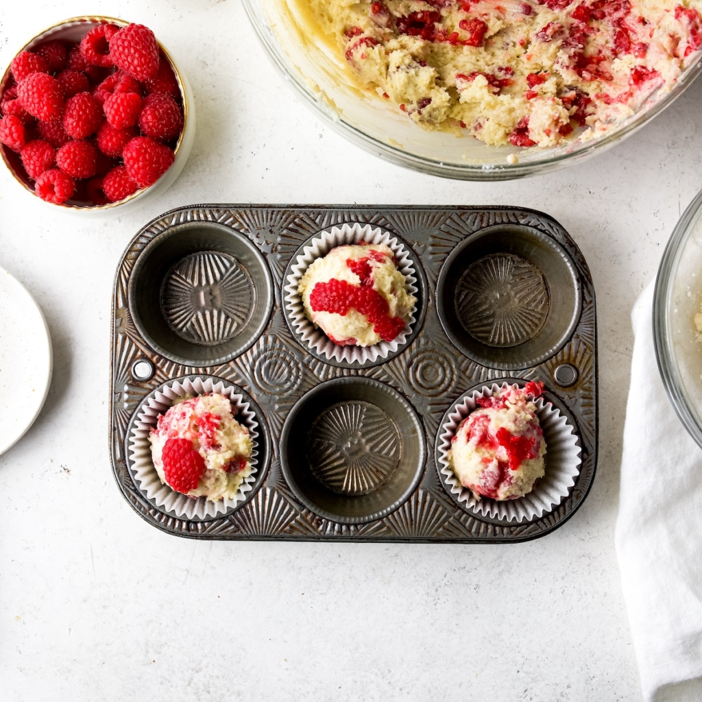 A muffin tin with muffin batter and raspberries.