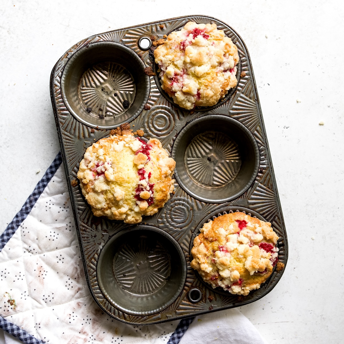 Three baked raspberry streusel muffins on a white surface.