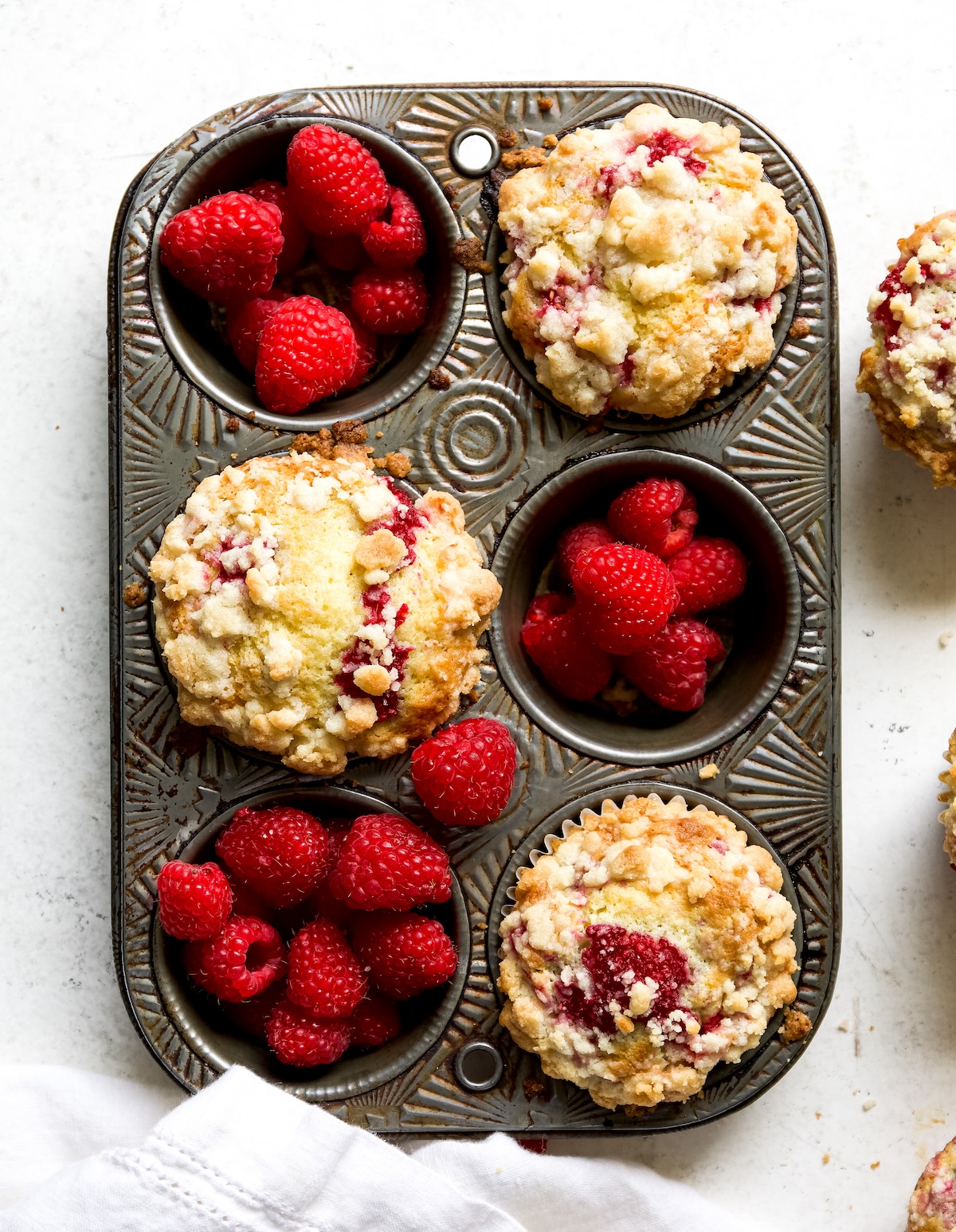 Three muffins in a muffin pan with fresh raspberries on a white background.