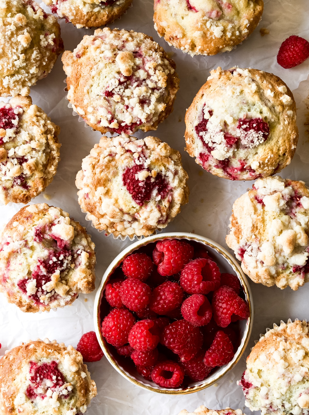 A bunch of Raspberry Muffins with streusel and a bowl of fresh aspberries.