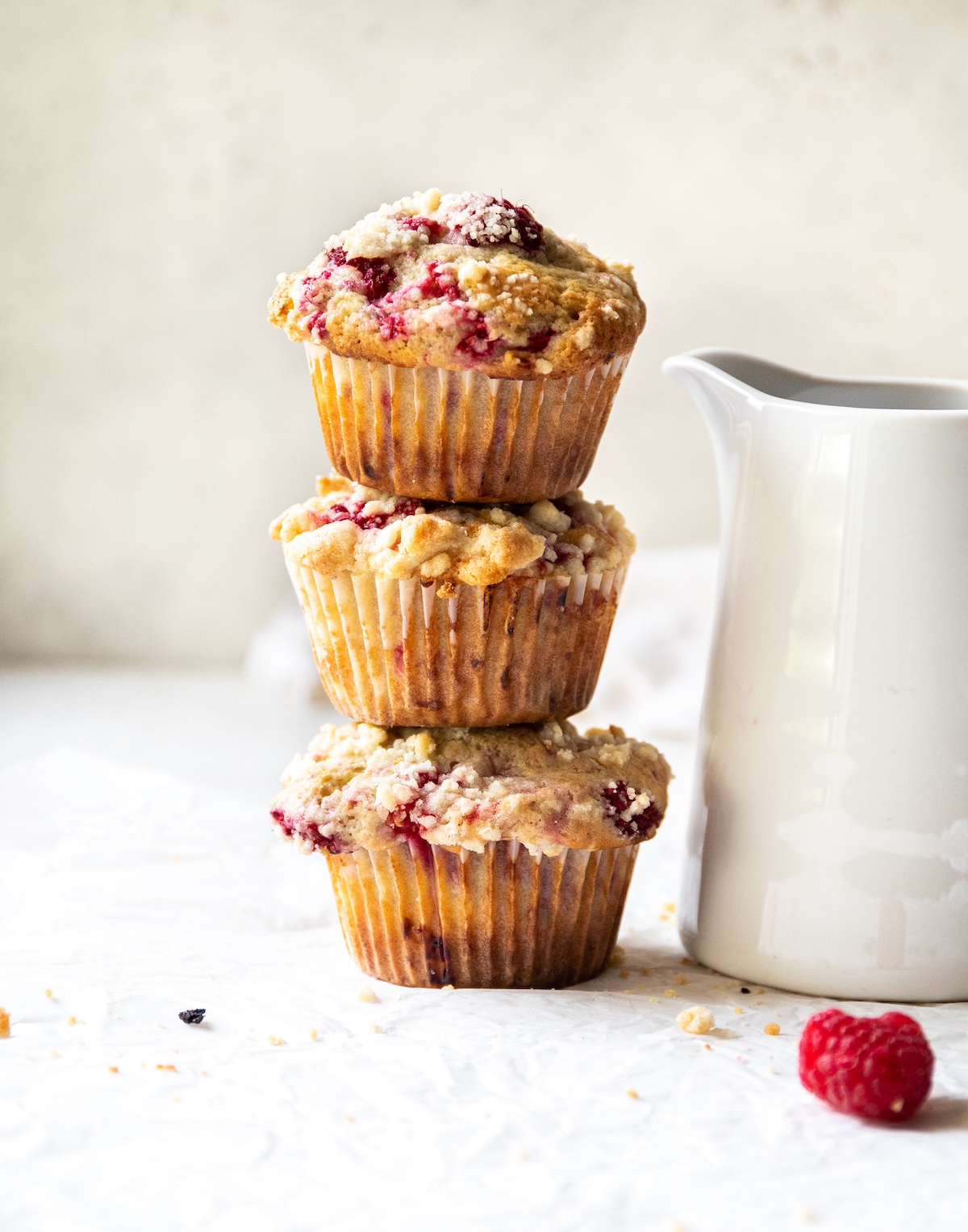 Three muffins stacked next to a white pitcher.